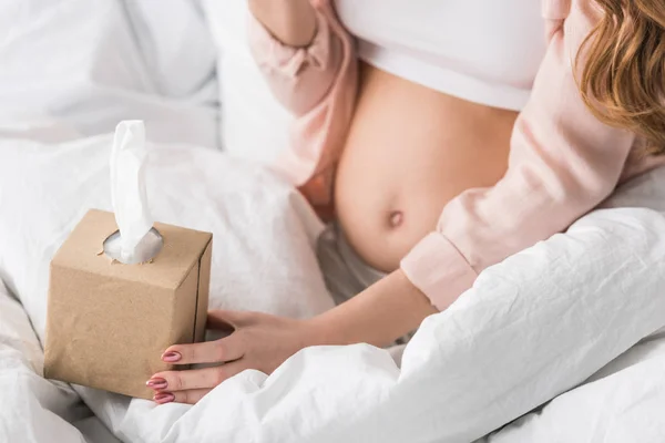 Vista recortada de la mujer embarazada sentada en la cama con servilletas - foto de stock
