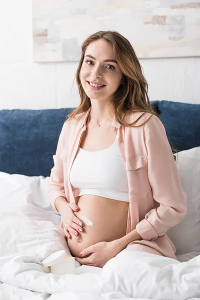 Smiling pregnant woman applying cream on belly — Stock Photo