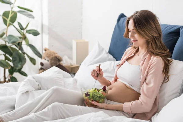 Charming pregnant woman eating fresh salad in bed — Stock Photo