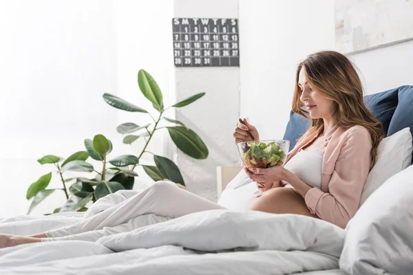 Belle femme enceinte mangeant de la salade au lit — Photo de stock