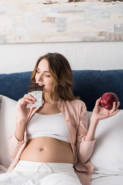 Schwangere hält Apfel und isst Schokolade — Stockfoto