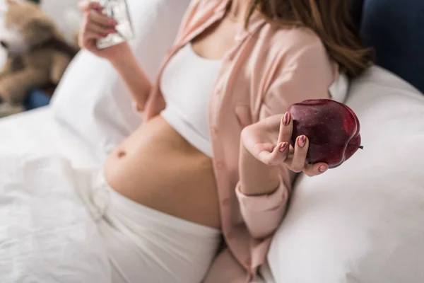 Partial view of pregnant woman holding red apple — Stock Photo