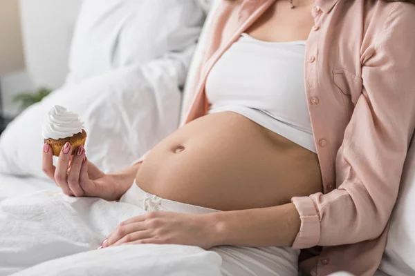 Vista parcial de la mujer embarazada con magdalena acostada en la cama - foto de stock