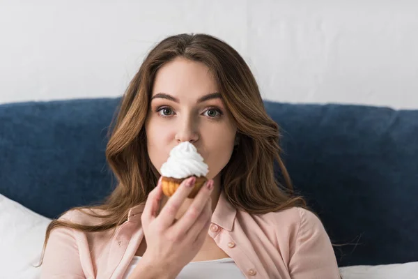 Morena hermosa mujer comiendo cupcake y mirando a la cámara - foto de stock