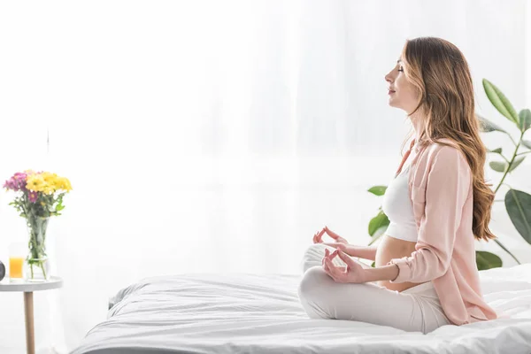 Vista lateral de la mujer embarazada meditando con los ojos cerrados - foto de stock