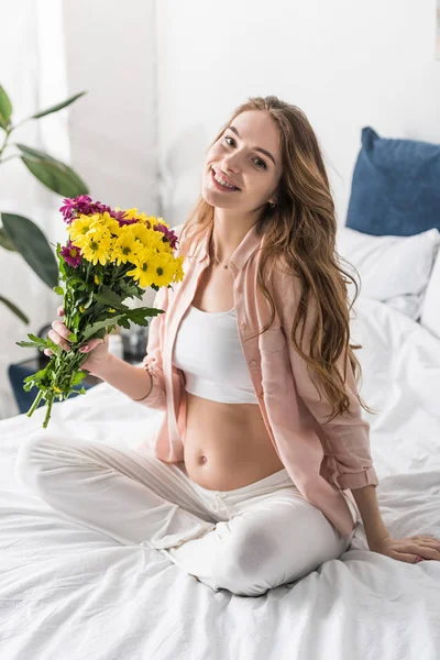 Mujer embarazada feliz sosteniendo flores y mirando a la cámara - foto de stock