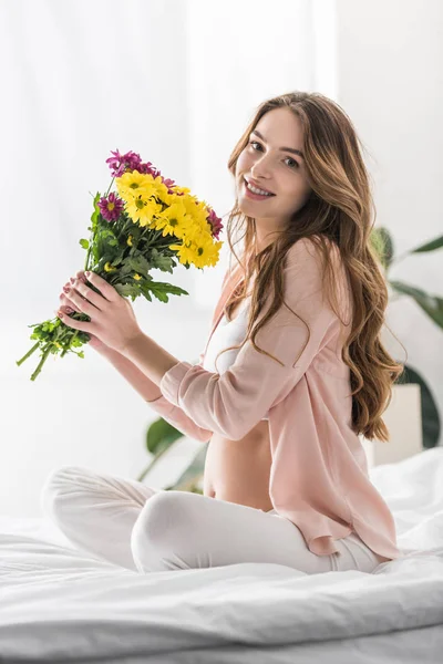 Donna incinta beata seduta sul letto con i fiori — Foto stock