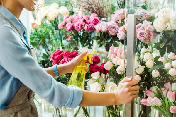 Cropped view of female florist spraying flowers with spray bottle in flower shop — Stock Photo