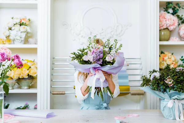 Fleuriste femelle tenant bouquet devant le visage au comptoir dans la boutique de fleurs — Photo de stock