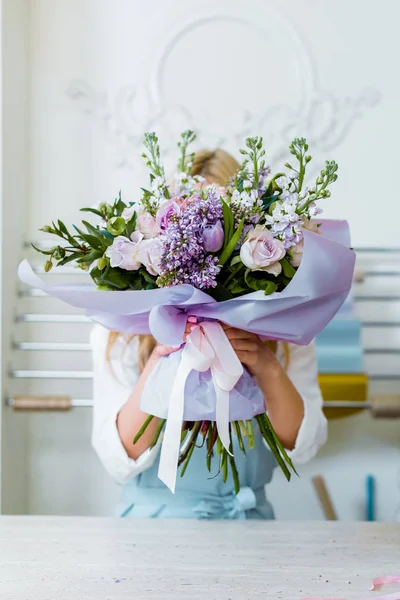 Woman holding flower bouquet with roses and lilac in front of face — Stock Photo