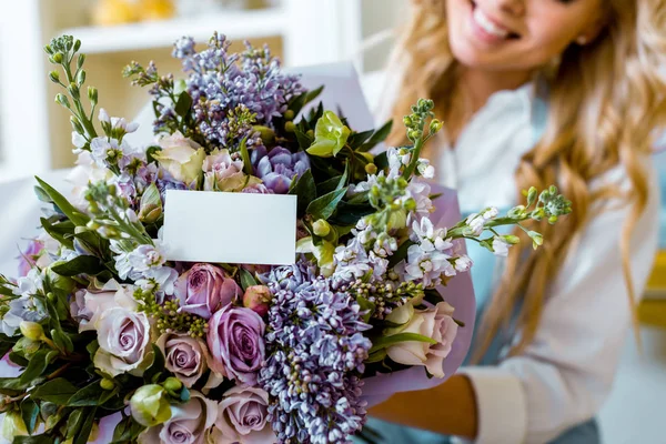 Vue recadrée d'une femme et bouquet de fleurs avec roses, lilas et carte avec espace de copie — Photo de stock