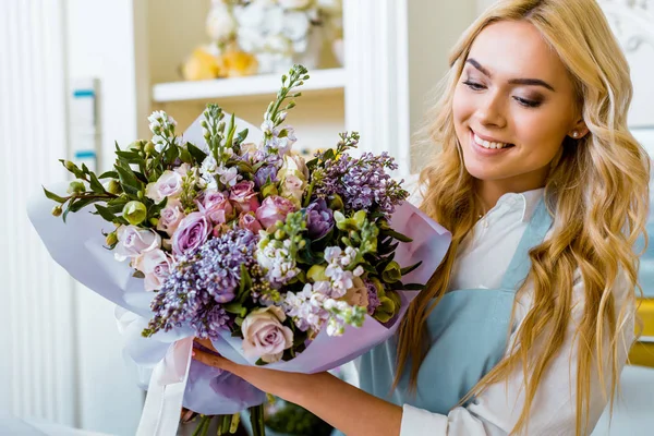 Selective focus of beautiful smiling female florist holding bouquet in flower shop — Stock Photo