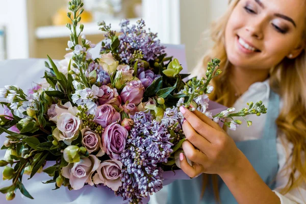 Florista femenina sonriente arreglo ramo con lila y rosas en floristería - foto de stock