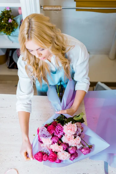 Hermosa florista femenina arreglando ramo con rosas y claveles en la tienda de flores - foto de stock