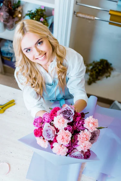 Belle fleuriste souriante arrangeant bouquet avec des roses et des œillets dans la boutique de fleurs — Photo de stock