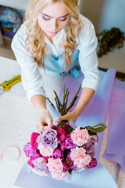 Bela florista feminina arranjando buquê com rosas e cravos na loja de flores — Fotografia de Stock