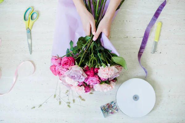 Vista superior do florista feminino que arranja buquê com rosas rosa e cravos na mesa — Fotografia de Stock