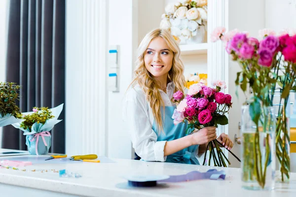 Beautiful smiling female florist holding pink bouquet in flower shop — Stock Photo