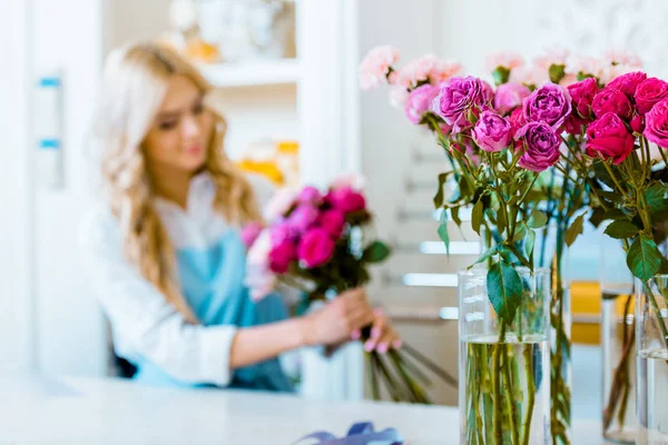 Fuoco selettivo di rose con fiorista femminile che organizza mazzo in negozio di fiori su sfondo — Foto stock