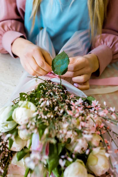 Partial view of female florist wrapping flower bouquet with white roses in paper — Stock Photo