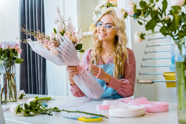 Foco seletivo da bela florista feminina em óculos arranjando buquê na loja de flores — Fotografia de Stock
