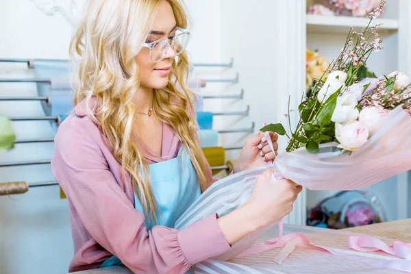 Bella fiorista femminile in bicchieri avvolgente bouquet in negozio di fiori — Foto stock