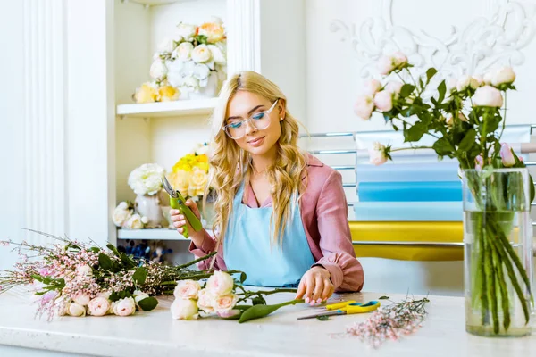 Bella fiorista femminile in bicchieri organizzare bouquet e tenere potatore in negozio di fiori — Foto stock