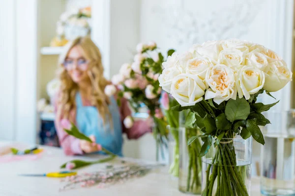 Selective focus of white roses with female florist in flower shop on background — Stock Photo