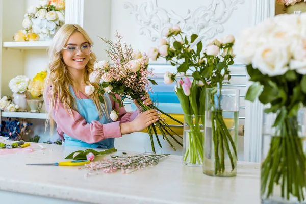 Bella fiorista femminile felice in bicchieri organizzare bouquet in negozio di fiori — Foto stock