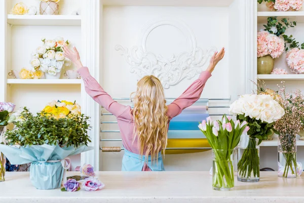 Back view of female florist with hands in air in flower shop — Stock Photo