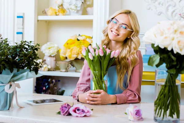 Bella fiorista donna felice che tiene vaso con tulipani rosa nel negozio di fiori — Foto stock