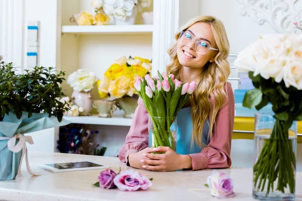 Schöne glückliche Blumenhändlerin hält Vase mit rosa Tulpen im Blumenladen — Stockfoto