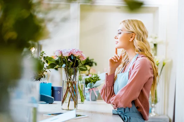 Beautiful female florist with bouquet of pink roses on counter in flower shop — Stock Photo