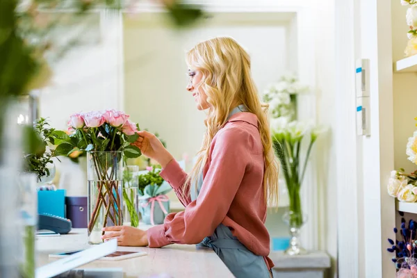 Hermosa florista femenina ajustando ramo de rosas rosadas en la tienda de flores - foto de stock