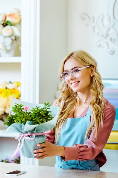 Bella fiorista femminile sorridente in bicchieri che presenta bouquet in negozio di fiori — Foto stock