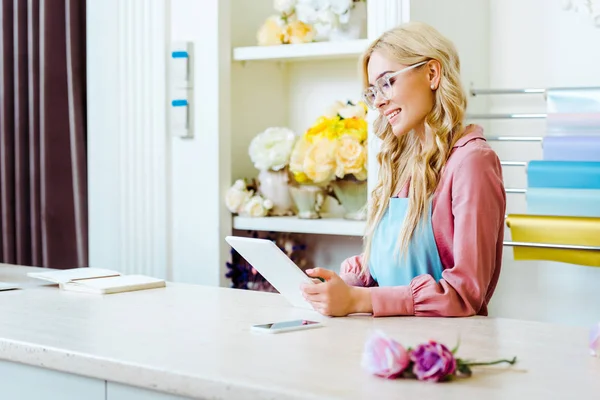 Beautiful female flower shop owner in glasses using digital tablet at counter — Stock Photo