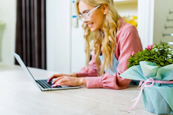 Селективный фокус цветочного букета с женщиной-флористкой с помощью ноутбука в цветочном магазине на заднем плане — стоковое фото