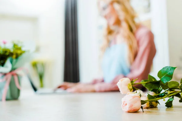 Selective focus of pink roses on desk with copy space and woman on background — Stock Photo