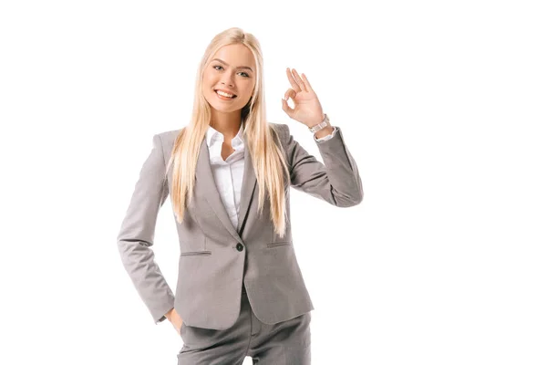 Hermosa mujer de negocios sonriente en traje mostrando signo ok aislado en blanco - foto de stock