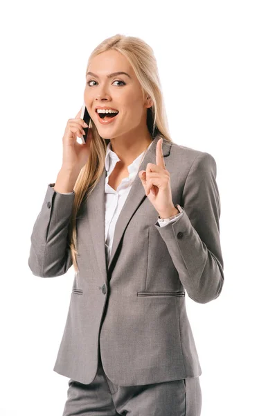 Mujer de negocios alegre teniendo idea y apuntando hacia arriba mientras habla en el teléfono inteligente aislado en blanco - foto de stock
