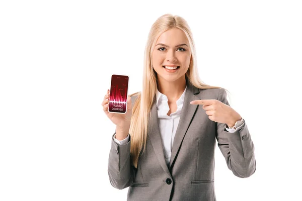 Lächelnde blonde Geschäftsfrau zeigt auf Smartphone mit Trading Courses App, isoliert auf Weiß — Stockfoto