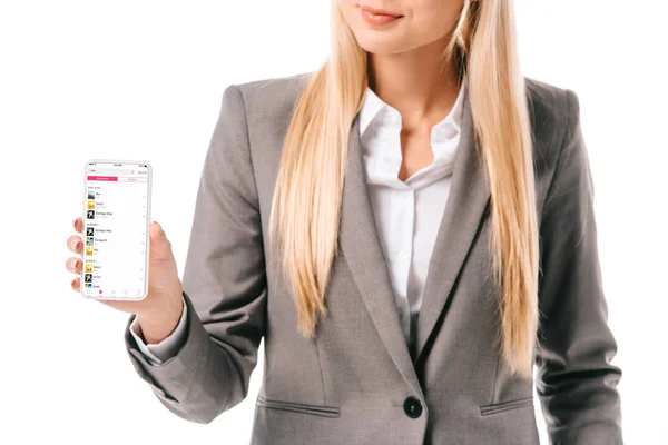 Vista recortada de la mujer de negocios que muestra el teléfono inteligente con aplicación de música de manzana, aislado en blanco - foto de stock