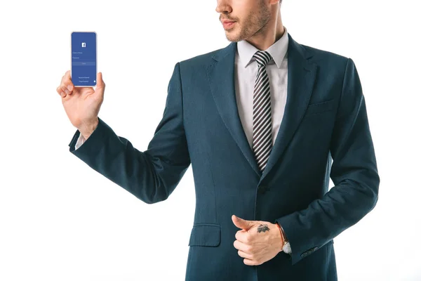 Vista recortada de hombre de negocios mostrando teléfono inteligente con aplicación de facebook, aislado en blanco - foto de stock