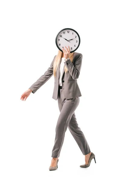 Femme d'affaires en costume gris tenant horloge devant le visage tout en marchant isolé sur blanc — Photo de stock