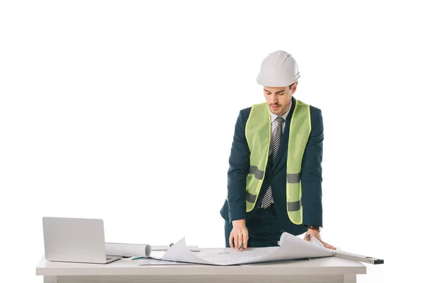 Arquitecto masculino en casco y chaleco de seguridad trabajando con planos y portátil, aislado en blanco - foto de stock