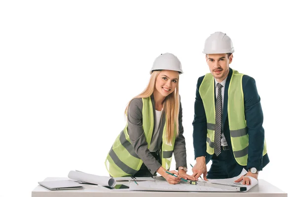 Ingenieros en chalecos de seguridad y cascos que trabajan con planos, aislados en blanco - foto de stock