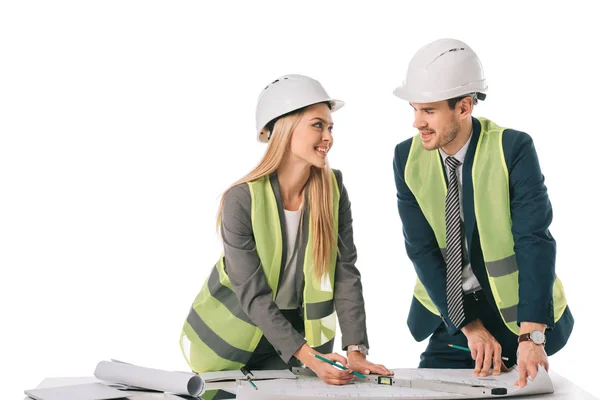 Arquitetos em coletes de segurança e hardhats trabalhando com plantas, isolados em branco — Fotografia de Stock