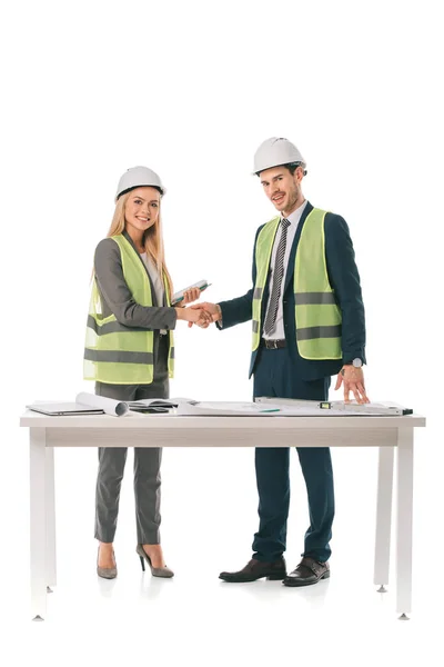Arquitectos en chalecos de seguridad y cascos estrechando las manos, aislados en blanco — Stock Photo