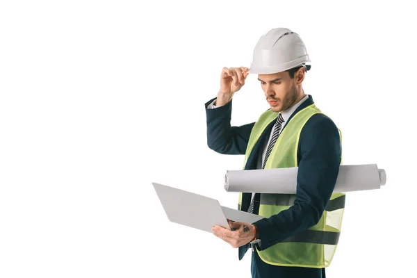 Engenheiro masculino em capacete e colete de segurança segurando planta e usando laptop, isolado em branco — Fotografia de Stock