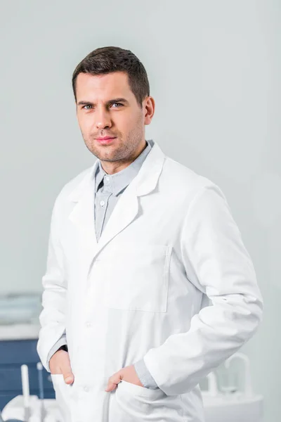 Красивий стоматолог стоїть з руками в кишенях у клініці — стокове фото